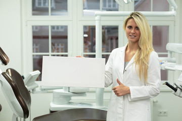 Obraz na płótnie Canvas Junge Frau / Zahnarzt Helferin hält weißes Schild vor Behandlung