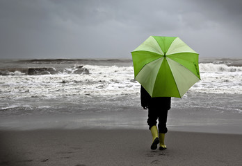 Niño bajo la lluvia en la playa con paraguas