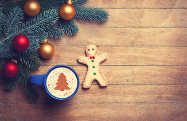 Cappuccino with gingerbread man and pine branch on wooden table.