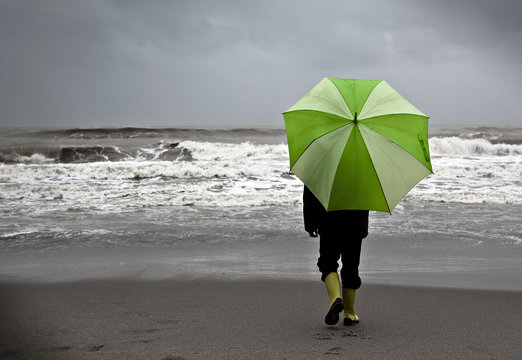 Ni&ntilde;o bajo la lluvia en la playa con paraguas