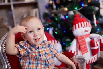 active, cheerful kid is sitting in a chair near the Christmas tr
