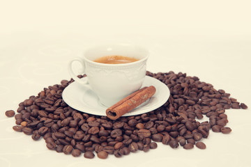 The cup of black coffee with grains and cinnamon stick, toned