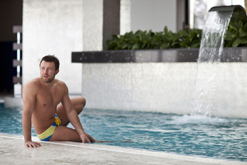 Young wet sexy muscular man posing in the swimming pool 