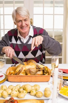 Portrait of a grandfather carving roast turkey at christmas