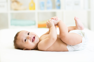 baby lying on white bed and holding legs - 74478868