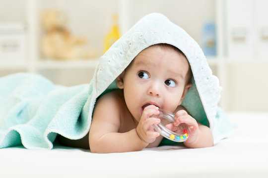Cute baby with teether under towel indoor