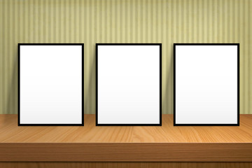 Three blank poster stand on a wooden table over vintage wallpape