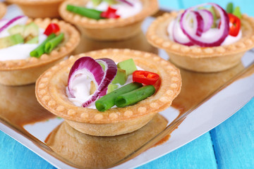 Tartlets with greens and vegetables with sauce on tray on table