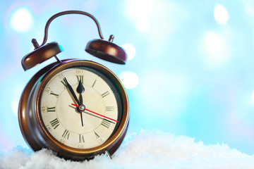 Alarm clock in snow on bright background