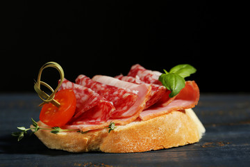 Tasty sandwich on wooden table, on black background
