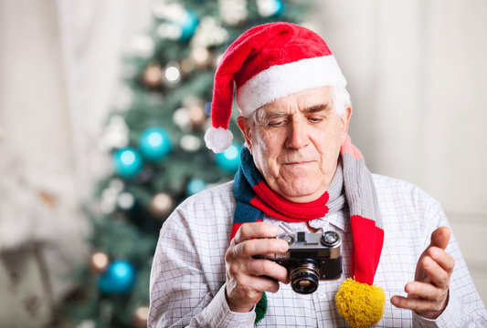Senior man in Santa hat looking at display of retro style camera
