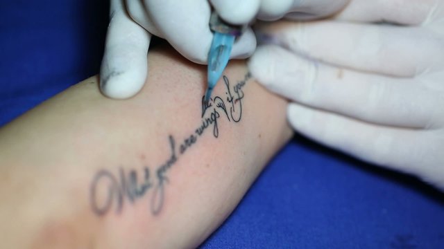 Tattoo master prints the letters to woman on his arm