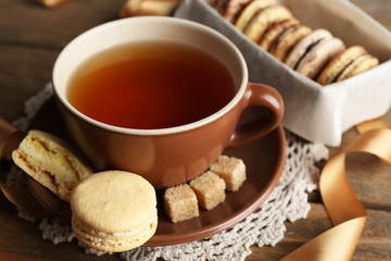 Colorful macaroons with cup of tea on wooden background
