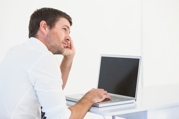 Thinking businessman sitting at desk using laptop