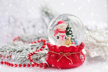 Fototapeta na wymiar A snow globe with snowman on background spruce branches with sno