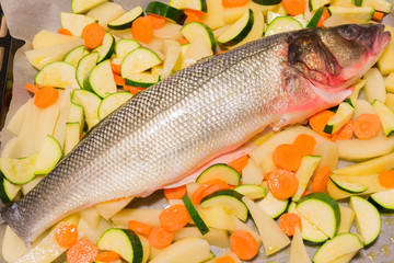 raw sea bass fish with sliced potatoes, carrots and zucchinis