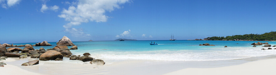 on the beach in front of the Seychelles white sail boat sails on