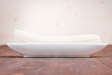 one peeled banana on a plate on a brown table side view