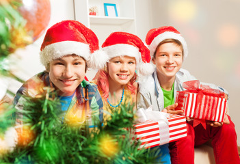 Cute teen children with presents by Christmas tree