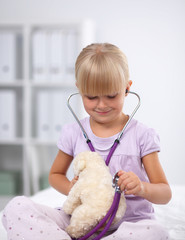 Little girl is examining her teddy bear using stethoscope