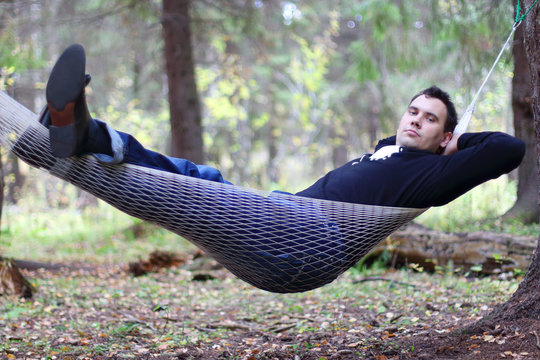 Handsome young man lies in hammock in woods at dull autumn day