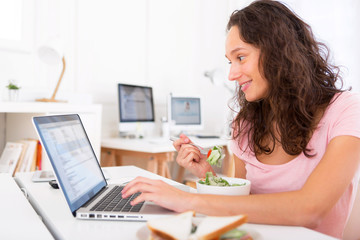 Young attractive student eating salad while working