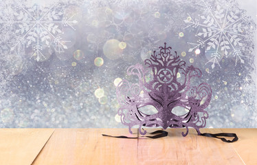 Mysterious Venetian masquerade mask on wooden table and glitter 