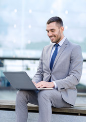 smiling businessman working with laptop outdoors