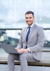 Fototapeta premium smiling businessman working with laptop outdoors