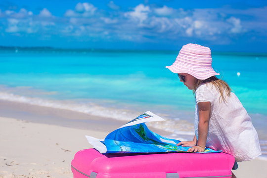Little adorable girl with big suitcase on tropical beach