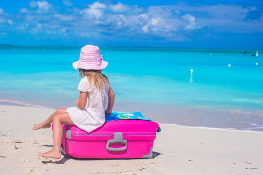 Little adorable girl with big suitcase on tropical beach