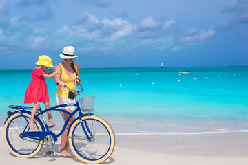 Obraz premium Happy mom and cute girl riding bicycles on tropical beach