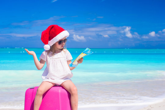 Little cute girl in Santa hat on suitcase at tropical beach