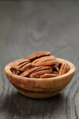 dried pecan nuts in olive bowl on wood table