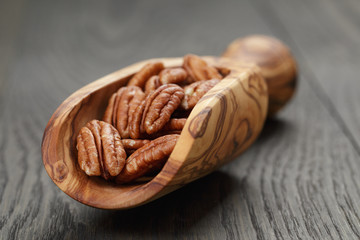 dried pecan nuts in olive scoop on wood table