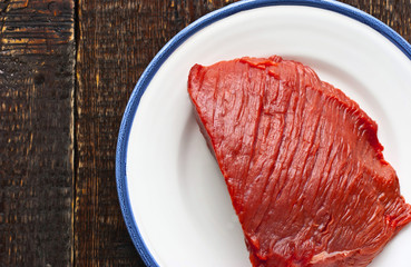 Raw red meat on the plate on the wooden table
