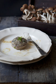 one stuffed mushroom on plate on table with raw mushrooms