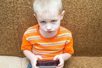 little boy sitting on the couch playing in the smartphone