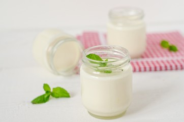Obraz na płótnie Canvas Homemade yogurt in glass jars with mint on white background.Selective focus