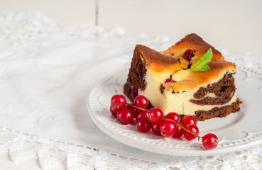 Cheesecake brownies with currant in white plate on wooden background. Slice of cake