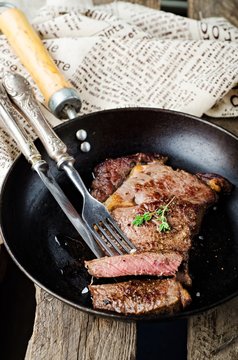 Roasted beef steak antrecot in iron pot on wooden vintage background. Slice of steak