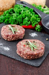 Fresh raw burger cutlets on slate stone black board and wooden background