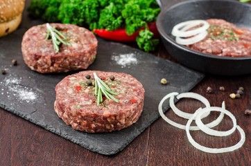 Fresh raw burger cutlets on slate stone black board and wooden background