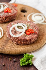 Raw burger cutlets with onion, peppers and parsley on wooden plate and wooden background