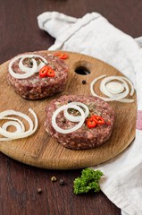 Raw burger cutlets with onion, peppers and parsley on wooden plate and wooden background