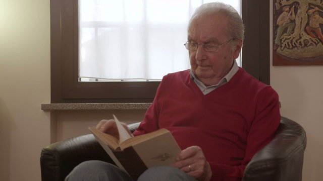 Elder man reading a book moves his eyeglasses to read better