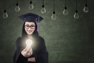 Attractive female graduate giving lit bulb under lamps