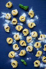 Raw tortellini over dark blue wooden surface, above view
