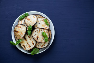 Glass plate with grilled aubergine slices and green basil leaves