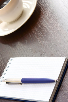A cup of coffee and a notebook with a pen on a wooden table